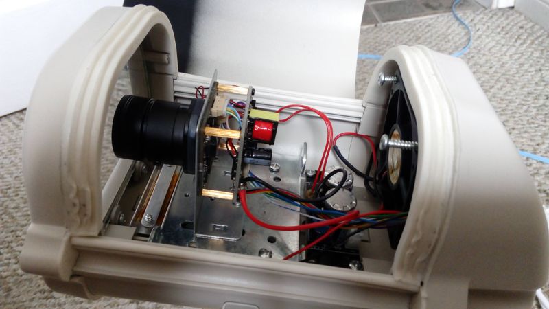 An opened camera housing showing a small lens, circuit boards and wiring